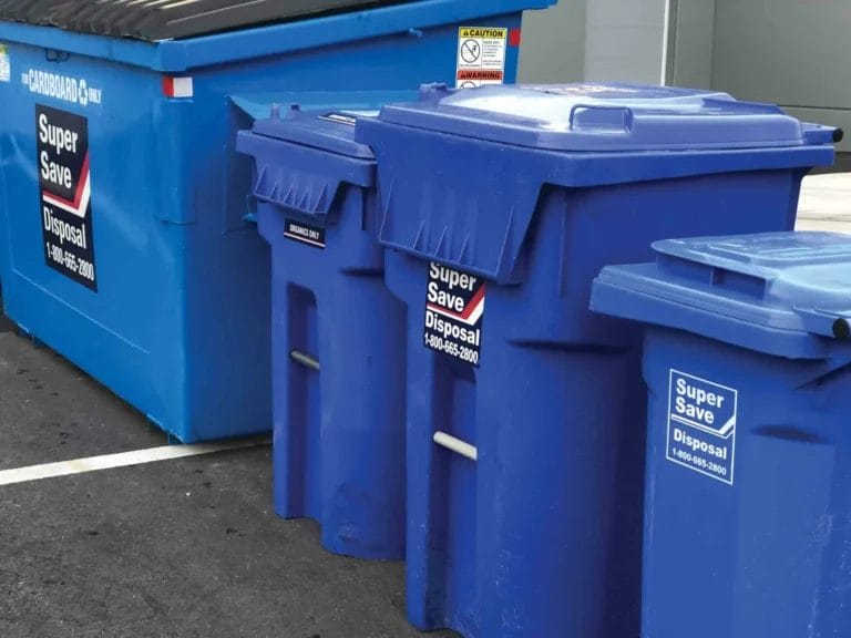 Four blue waste disposal bins labelled "Super Save Disposal" are lined up next to a larger blue dumpster with similar labelling in an outdoor setting