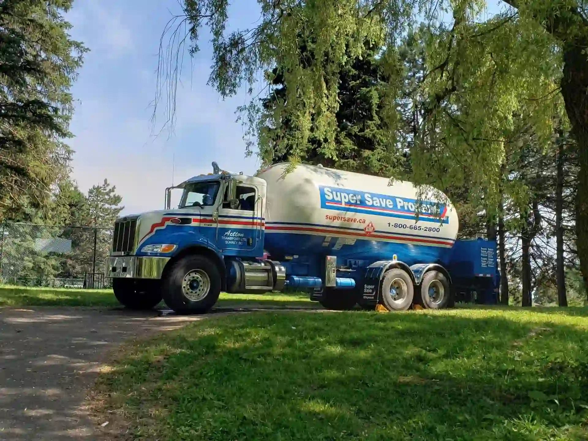 A large truck with a white and blue tank, labelled "Super Save Propane," parked on a gravel path surrounded by trees.