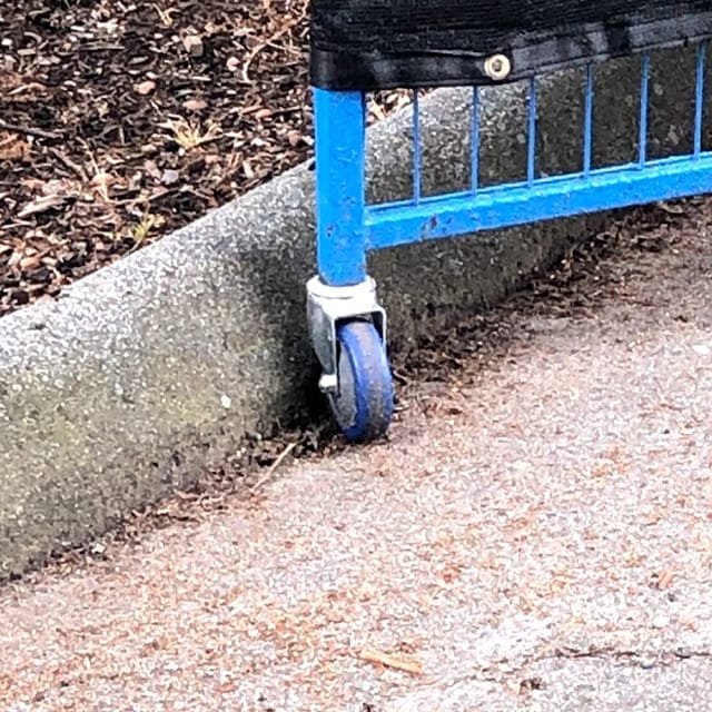 Close-up of a blue caster wheel attached to a metal gate positioned on a concrete curb